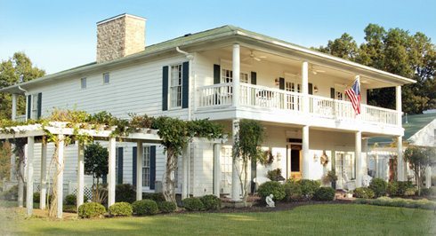front view of a large white colonial style home with wrap around porch